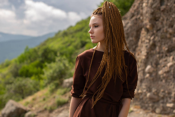 A girl with red cornrows poses in a profile against the backdrop of nature - Foto, afbeelding