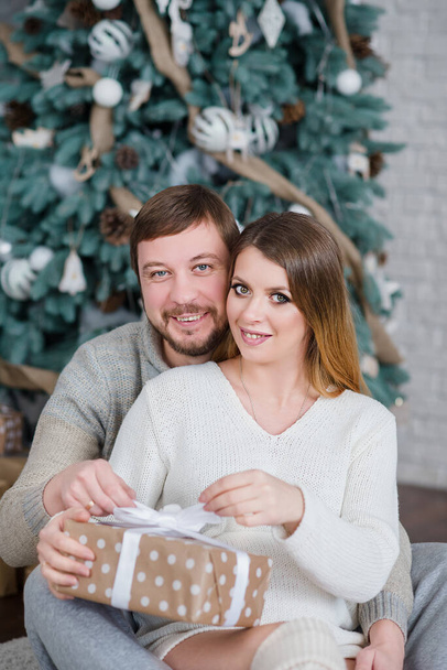 Young happy couple near Christmas tree. Happy young people give each other gifts by fireplace. New Year present box. Concept happy celebration of Christmas and New Year holidays - Foto, imagen