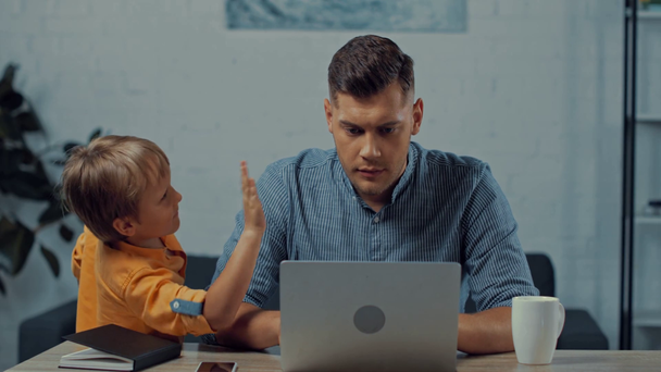 figlio disturbare padre occupato utilizzando il computer portatile mentre si lavora da casa - Filmati, video