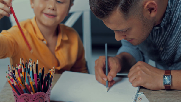 Baba ve oğlunun renkli kalemlerle kağıda çizimlerinin seçici odak noktası - Video, Çekim