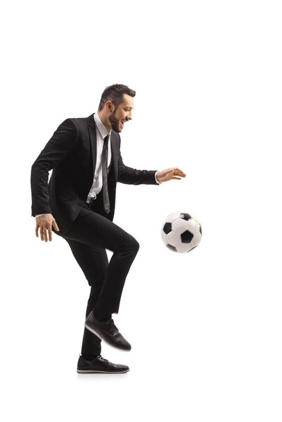 Full length profile shot of a man in a suit kicking a football isolated on white background - Valokuva, kuva