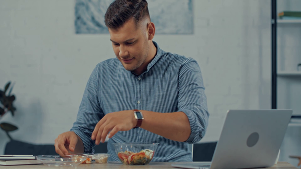 pohledný freelancer pomocí notebooku a jíst salát - Záběry, video