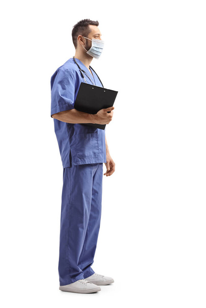 Perfil de comprimento total tiro de um trabalhador médico em um uniforme azul com uma máscara facial isolada no fundo branco
 - Foto, Imagem