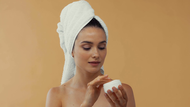Chica desnuda en toalla en la cabeza aplicando crema anti edad aislado en beige
 - Imágenes, Vídeo