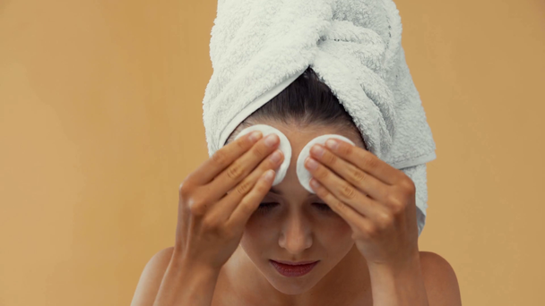 Γυμνός κορίτσι με πετσέτα στο κεφάλι καθαρισμού πρόσωπο με βαμβάκι μαξιλάρια απομονώνονται σε μπεζ - Πλάνα, βίντεο