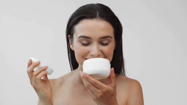 Smiling naked girl smelling cosmetic cream in container isolated on grey - Footage, Video