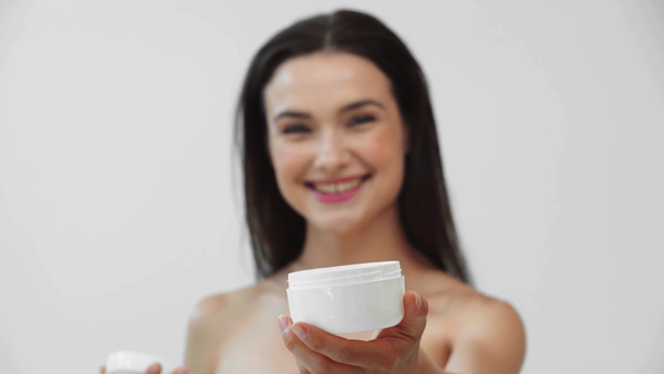 Nackte Frau lächelt und zeigt Container mit Kosmetikcreme isoliert auf grau - Filmmaterial, Video