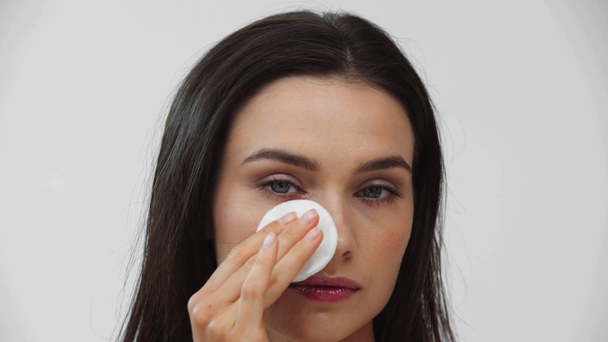 Kobieta czyści twarz podkładką bawełnianą i uśmiecha się odizolowana na szaro - Materiał filmowy, wideo