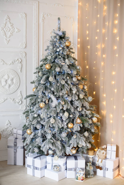 snowbound Christmas tree with golden toys in the interior against the background of white stucco molding with bokeh. - Фото, зображення