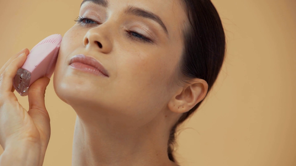 piękna kobieta za pomocą silikon twarzy brash izolowane na beżowy - Materiał filmowy, wideo