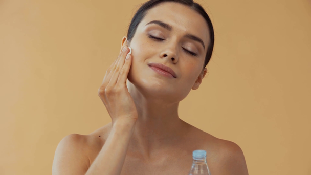 Schöne nackte Frau, die Make-up-Entferner isoliert auf beige aufträgt - Filmmaterial, Video