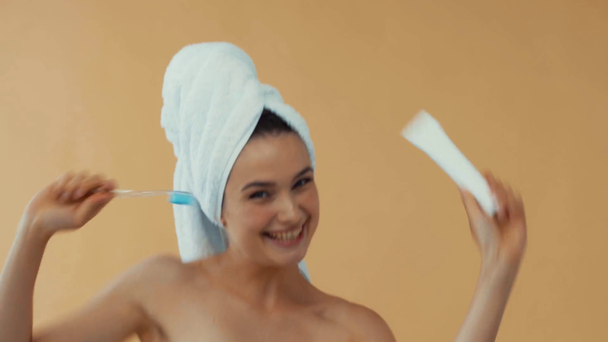 Mujer sonriente en toallas bailando con cepillo de dientes y pasta de dientes aislados en beige
 - Imágenes, Vídeo