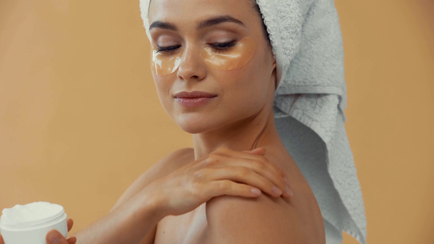 Schöne Frau mit Handtuch auf dem Haar Anwendung kosmetischer Creme isoliert auf beige - Filmmaterial, Video