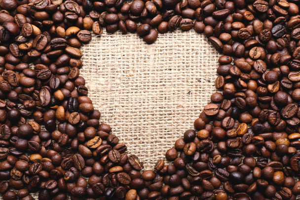 Heart shaped frame made from coffee beans on linen cloth - Photo, Image