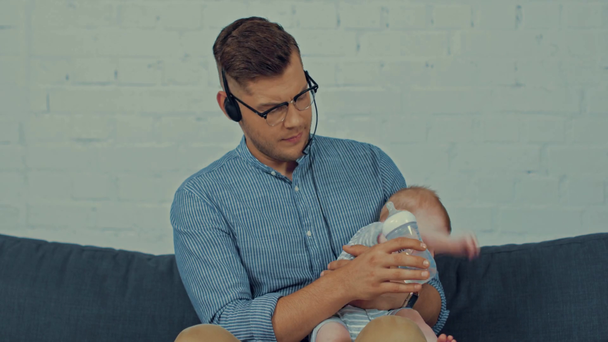 ojciec w słuchawki pracy z domu i karmienia słodkie niemowlę chłopiec  - Materiał filmowy, wideo