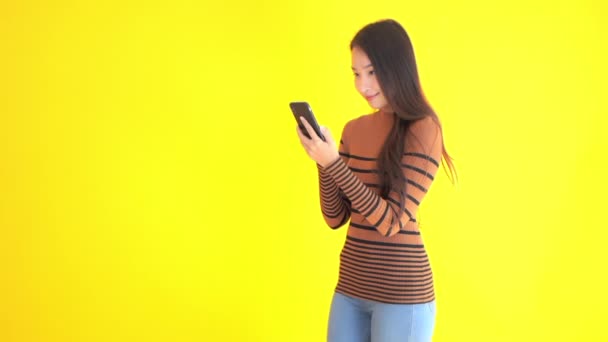 close-up footage of beautiful young Asian woman using smartphone isolated on yellow - Footage, Video