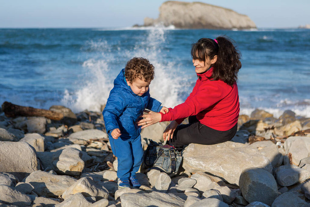 Anne ve oğlu öğleden sonralarını deniz kenarındaki kayalıklarda geçiriyor. - Fotoğraf, Görsel