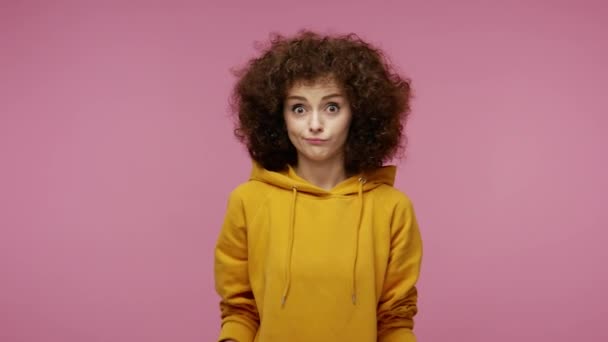 Don't know what to say! Confused unsure girl afro hairstyle in hoodie shrugging shoulders feeling embarrassed about ambiguous question, having doubts. indoor studio shot isolated on pink background - 映像、動画