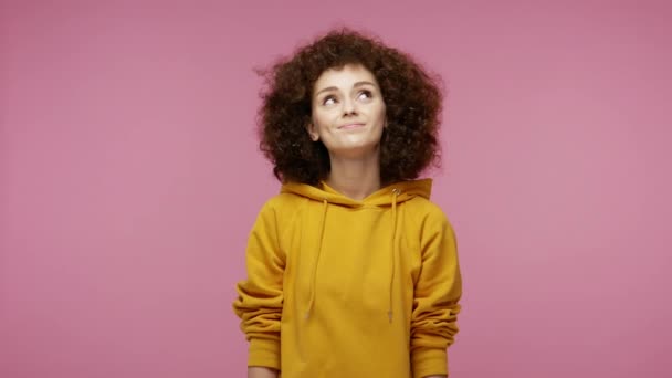Lovely pensive woman afro hairstyle in hoodie dreaming with happy meditative expression, fantasizing enjoying pleasant memories, girlish hopes and wishes. studio shot isolated on pink background - Felvétel, videó