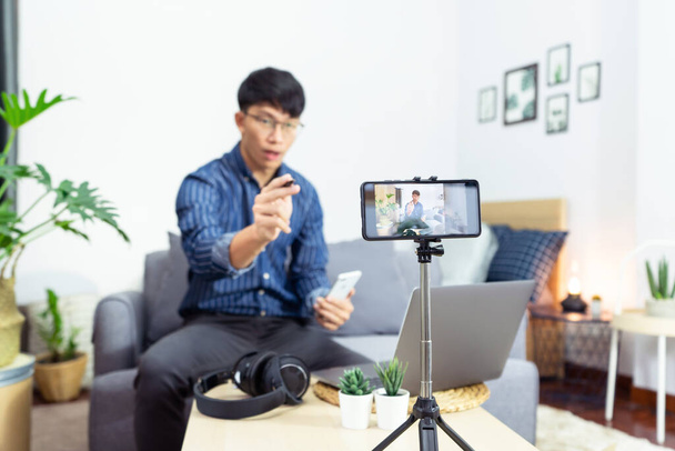 Молодой азиат мужчина блоггер запись видео видеосъемки на камеру обзор продукта в домашнем офисе, фокус на штатив установлен камера экран транслировать прямой трансляции видео в социальной сети - Фото, изображение