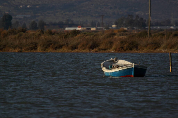Маленькое старое рыбацкое судно, брошенное в реке. В реке есть деревянные столбы и тростник на берегах. Фотография сделана в устье реки на юге Турции.. - Фото, изображение