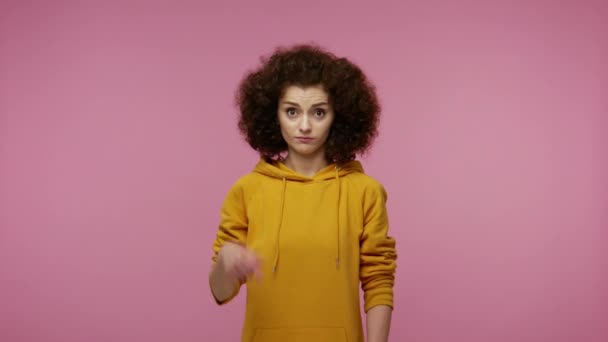 You are dumb idiot! Girl afro hairstyle in hoodie showing stupid gesture and pointing to camera, accusing crazy cuckoo mind, blaming insane idea, reckless plan. studio shot isolated on pink background - Πλάνα, βίντεο