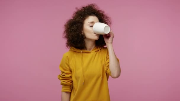 Dental problems. Girl afro hairstyle in hoodie drinking hot or ice water and feeling sudden terrible toothache, pain from sensitive tooth and cavities. indoor studio shot isolated on pink background - Video