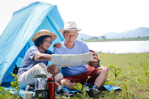 Dos amantes ancianos acampando en el bosque Sentados y mirando el mapa de papel para estudiar las rutas de senderismo. El concepto de relajación senior
 - Foto, imagen