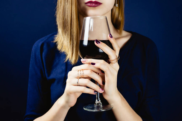 Faceless portrait of young adult white woman wearing dark plum lipstick holding a glass of red wine in her hands. Selective focus. - 写真・画像