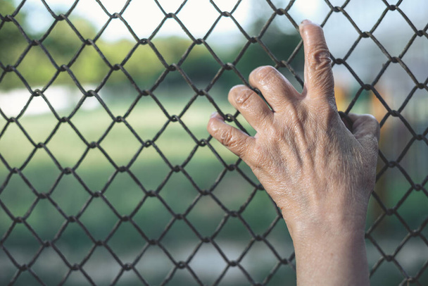 Fili di recinzione a catena afferrati a mano da un anziano. Fuggire da un paese pieno di violenza in uno piu 'sicuro. Concetto di immigrazione - Foto, immagini
