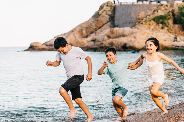 Trois enfants drôles courent sur la plage - Photo, image