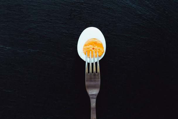 Organikus tojás fele villával a tetején elhelyezett kő texturált háttér. Egészséges és természetes, fehérjékkel teli ételek reggelire. - Fotó, kép