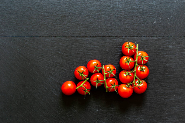 Branch of red ripe cherry tomatoes placed in a corner on a black background with copy space. Organic vegetables for healthy and balanced vegetarian diet - Photo, Image