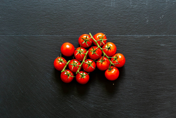 Siyah arkaplanın ortasında kiraz domatesleri dalları. Sağlıklı beslenmek için besin ve vitamin dolu olgun organik sebzeler. - Fotoğraf, Görsel