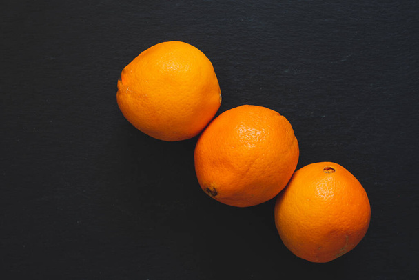 Közelkép narancsokról átlós vonalban, fekete alapon. Szaftos trópusi citrusfélék, tele vitaminokkal, kőzetszerkezetű palán - Fotó, kép