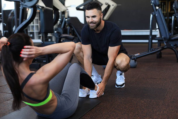 Trainer helping young woman to do abdominal exercises in gym - Photo, Image