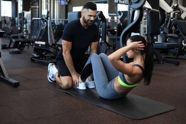 Valmentaja auttaa nuorta naista tekemään vatsan harjoituksia kuntosalilla - Valokuva, kuva