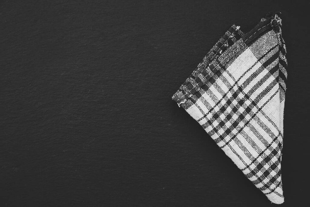 Black and white plaid rustic towel folded in a triangle shape on a black background with copy space. Kitchen cloth made from thin fabric for protection against heat - Photo, Image