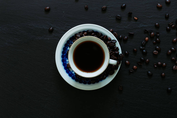 Кружка с ароматом арабского языка с небольшим количеством семян кофе на черном фоне. Вид сверху и крупный план черного кофе на столе
. - Фото, изображение