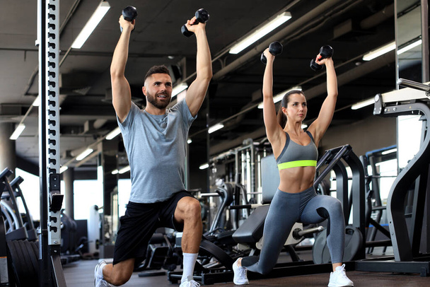 Attractive sports people are working out with dumbbells at gym - Photo, Image