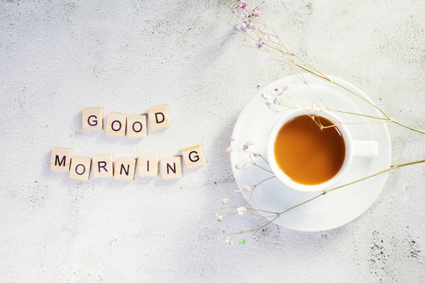 Delicious coffee with milk and text GOOD MORNING wish on light gray background, flat lay, copy space - Photo, Image