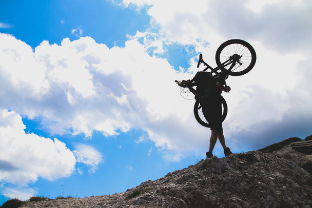 sport man in action lifting bike on his shoulder on rock mountain with blue sky background. - Photo, Image
