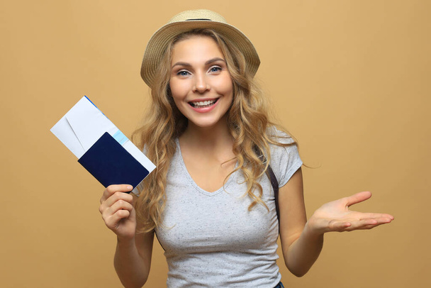 Beautiful blonde woman wearing summer clothes posing with passport with tickets over beige background - Foto, afbeelding