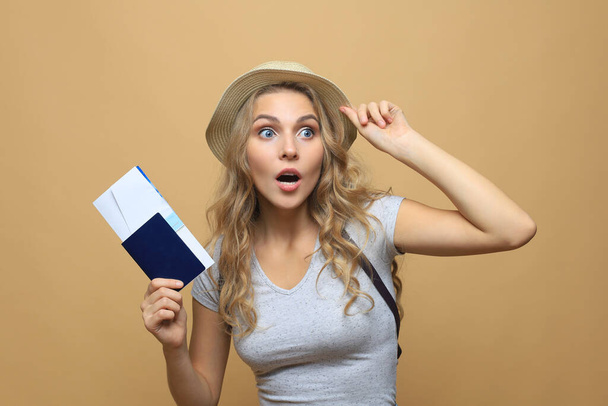 Beautiful blonde woman wearing summer clothes posing with passport with tickets over beige background - Foto, Bild
