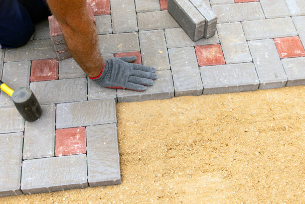 Hände eines Arbeiters in Handschuhen, der Betonblöcke mit einem Gummihammer verlegt - Foto, Bild