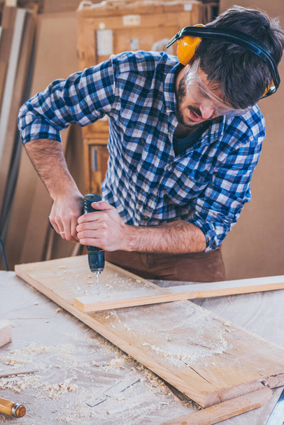 Carpinteiro no trabalho usando broca de mão
 - Foto, Imagem