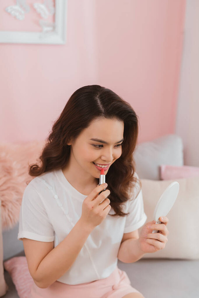 beautiful young woman putting on red lipstick - Foto, Bild
