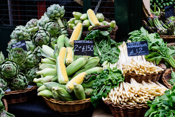Verduras ecológicas verdes en exhibición para la venta en un mercado callejero de alimentos, con nombres mostrados en inglés, espárragos blancos, alcachofa, maíz amarillo dulce, de una granja
 - Foto, imagen