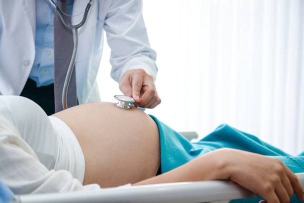 Il medico ha usato uno stetoscopio a campana per controllare la gravidanza di una donna sdraiata in un letto in una clinica.. - Foto, immagini