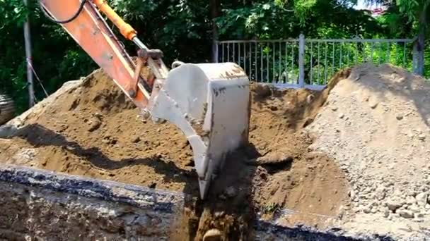 Excavator puts soil into the trench. Laying pipes in the ground, backfilling with sand pits. Street of the city. Day. Summer. Georgia. - Footage, Video